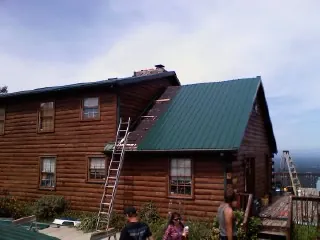 Green metal roof going on a two story log home with ladders set in Macon